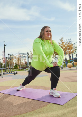 Energetic obese young woman in warm sportswear workout at sportsground in spring sunny day. Concept of challenges, dreams, fitness, healthy lifestyle Energetic obese young woman in warm sportswear workout at sportsground in spring sunny day. Concept of challenges, dreams, fitness, healthy lifestyle 95701703