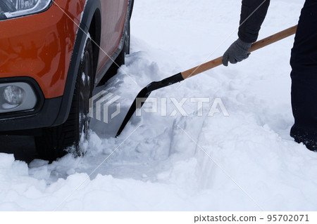 Winter, snow, vehicle. Man brushing and shoveling snow beside orange car in winter after snowfall. Shovel in hand. 95702071