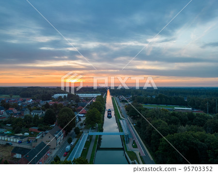Aerial view of a colourful dramatic sunrise sky over a canal with a cargo boat in Belgium. Canals Aerial view of a colourful dramatic sunrise sky over a canal with a cargo boat in Belgium. Canals 95703352
