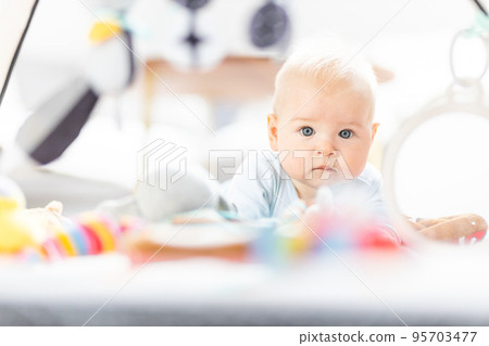 Cute baby boy playing with hanging toys arch on mat at home Baby activity and play center for early infant development. Baby playing at home 95703477