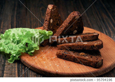 lettuce leaves and rye bread with pine nuts on a wooden board. lettuce leaves and rye bread with pine nuts on a wooden board. 95704196