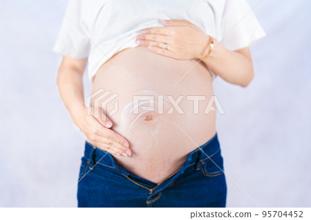 Pregnant woman wearing casual clothes and applying cream to prevent stretch marks Front view (shooting a real pregnant woman) 95704452