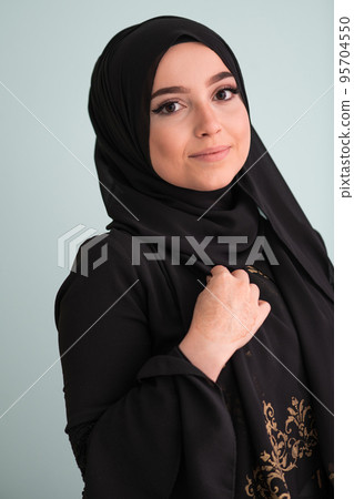 beautiful muslim woman in fashinable dress with hijab isolated on modern cyan background representing concept of modern islam and ramadan kareem 95704550