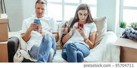 young couple with smartphones sitting on the sofa in a new apartment . 95704711