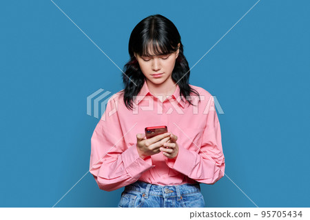 Sad female looking at smartphone screen, on blue color background Sad female looking at smartphone screen, on blue color background 95705434