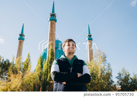 Looking away young unshaven beard man 34 years old against Muslim Mosque (Mashkhur Jusup Central Mosque) and yellow autumn leaves trees. Waist up lifestyle travel portrait, religion and trip concept. 95705730