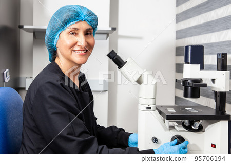 Female scientist looking at slides with patient samples using an inverted microscope in the laboratory. 95706194