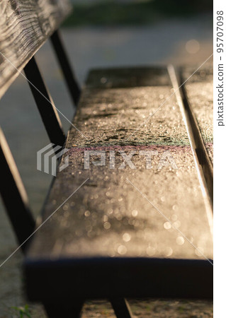 Early in the morning, the bench for the performance after the rain. The drops of water on the bench glisten in the morning sun. 95707098