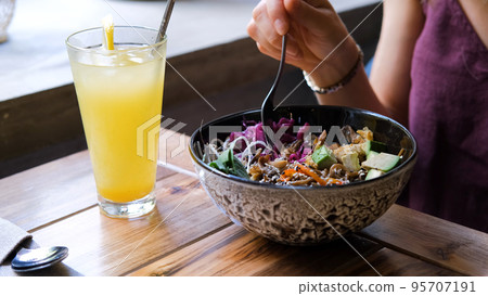 Closeup of young woman eating organic vegan poke bowl with fresh vegetables at restaurant or cafe. Healthy lifestyle and natural organic vegetarian food concept Closeup of young woman eating organic vegan poke bowl with fresh vegetables at restaurant or cafe. Healthy lifestyle and natural organic vegetarian food concept 95707191