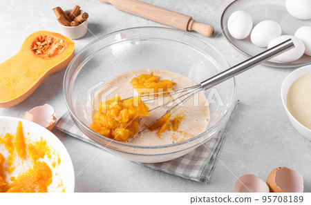 Bowl with pumpkin pie filling and whisk with ingredients for baking a pie on a gray table in the kitchen Bowl with pumpkin pie filling and whisk with ingredients for baking a pie on a gray table in the kitchen 95708189