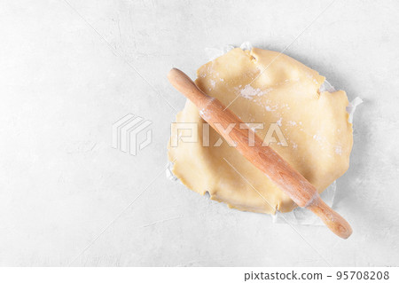 Raw crust pie dough into a baking dish with a rolling pin on a light gray background, pie crust recipe, above view Raw crust pie dough into a baking dish with a rolling pin on a light gray background, pie crust recipe, above view 95708208