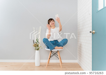 Asian woman making a video call and selfie with a smartphone (waving her hand) Asian woman making a video call and selfie with a smartphone (waving her hand) 95710263