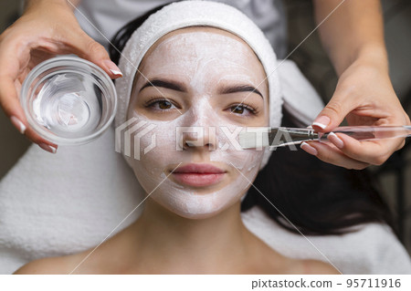 Close-up shot of a woman getting facial treatment with clay mask. Cosmetology and spa 95711916