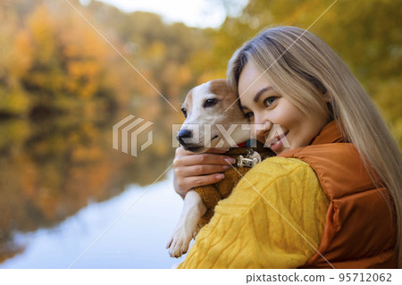 Portrait of a smiling young woman kissing a dog in a field. Dog lover stylish girl hugging her dog while walking. Animal friendship concept 95712062