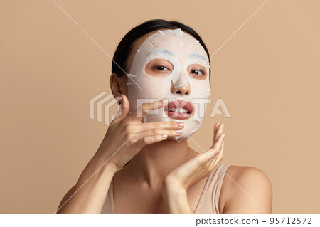 Woman Face Mask. Portrait Of Beautiful Girl Applying Cosmetic White Textile Mask 95712572
