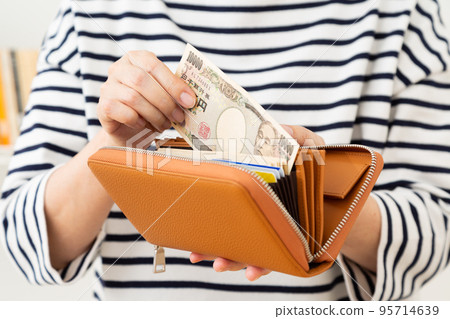 一名中年婦女，外表隨意，從錢包裡掏出錢來 95714639