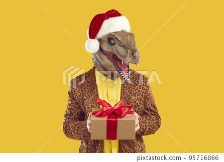 Funny dinosaur guy in Christmas hat and leopard suit holding Christmas present box 95716866