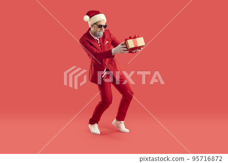 Funny man in red Xmas suit walks on tiptoes and secretly leaves Christmas present Funny man in red Xmas suit walks on tiptoes and secretly leaves Christmas present 95716872
