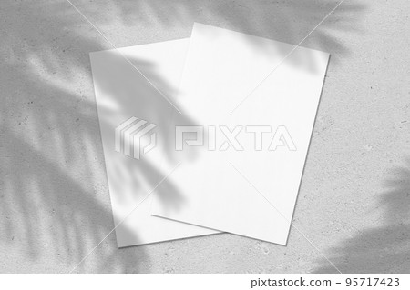 Two empty white vertical rectangle poster or card mockups with palm leaves shadows Two empty white vertical rectangle poster or card mockups with palm leaves shadows 95717423