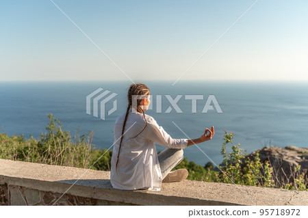 Profile of a woman doing yoga in the top of a cliff in the mountain. Woman meditates in yoga asana Padmasana Profile of a woman doing yoga in the top of a cliff in the mountain. Woman meditates in yoga asana Padmasana 95718972