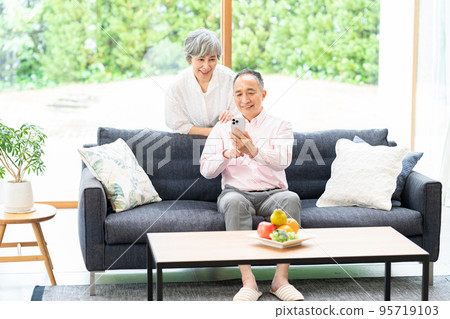Senior couple looking at a smartphone in the living room Senior couple looking at a smartphone in the living room 95719103
