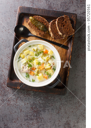 Polish creamy soup with pickled cucumbers, meat and vegetables close-up in a saucepan. Vertical top view Polish creamy soup with pickled cucumbers, meat and vegetables close-up in a saucepan. Vertical top view 95720561