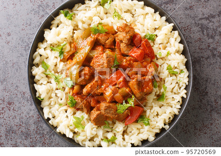 Porkolt is Hungarian for beef stew made by braising meat and simmering it with onions, paprika in a tomato based sauce served with Egg Noodles Nokedli closeup on the plate. Horizontal top view 95720569