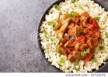 Porkolt is a Hungarian stew with boneless meat, paprika and some vegetables served with Egg Noodles Nokedli closeup on the plate. Horizontal top view 95720570