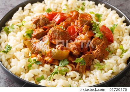 Porkolt is a Hungarian stew with boneless meat, paprika and some vegetables served with Egg Noodles Nokedli closeup on the plate. Horizontal 95720576
