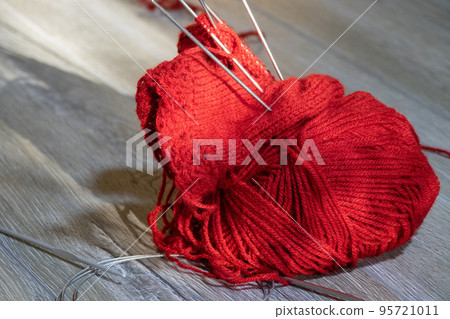 Sock in the process of knitting with needles and yarn of red color on a gray wooden table 95721011