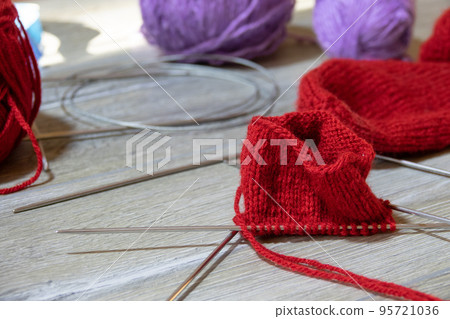 Sock in the process of knitting with needles and yarn of red color on a gray wooden table 95721036
