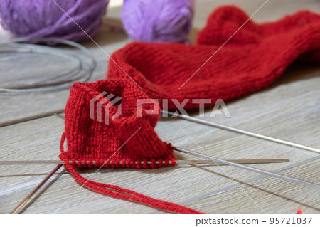 Sock in the process of knitting with needles and yarn of red color on a gray wooden table Sock in the process of knitting with needles and yarn of red color on a gray wooden table 95721037