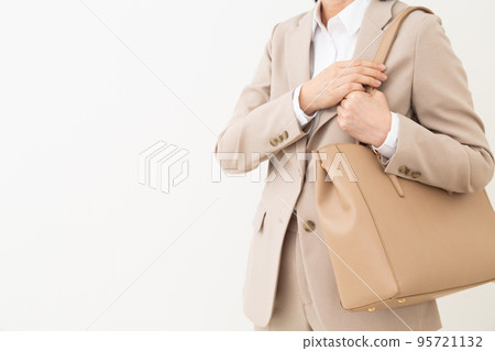 A middle-aged woman wearing a beige suit and white Y-shirt and holding a bag 95721132