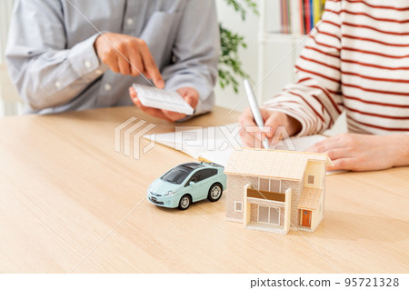 A middle-aged couple who calculates the household budget and a model of a car and a house A middle-aged couple who calculates the household budget and a model of a car and a house 95721328