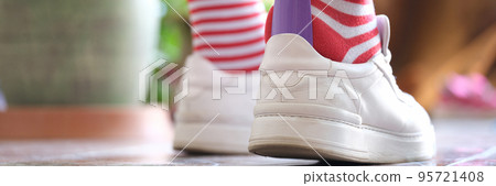 Man in striped socks putting on white sneakers with shoehorn closeup Man in striped socks putting on white sneakers with shoehorn closeup 95721408