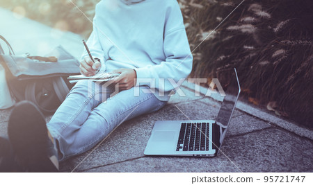 Man writing notebook with laptop in the park vintage style, Slim hipster man in jeans using a notebook, Freelancers, communication, Teenage student boy browses the Internet, working outside the home Man writing notebook with laptop in the park vintage style, Slim hipster man in jeans using a notebook, Freelancers, communication, Teenage student boy browses the Internet, working outside the home 95721747