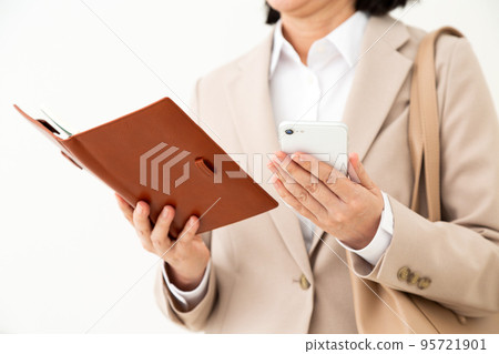 一位穿著西裝的中年婦女,帶著筆記本和智能手機 一位穿著西裝的中年婦女,帶著筆記本和智能手機 95721901