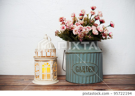 White lantern with rose flowers bouquet in metal vase on wooden shelf home decoration 95722194