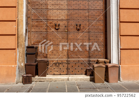 Brown plastic bins with biological waste on the sidewalk in front of a historic old wooden door. Brown plastic bins with biological waste on the sidewalk in front of a historic old wooden door. 95722562