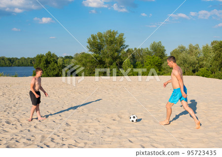 The concept of sports and active games in the summer. Father and son play with a ball on the beach. Beach soccer, vacation, lifestyle The concept of sports and active games in the summer. Father and son play with a ball on the beach. Beach soccer, vacation, lifestyle 95723435