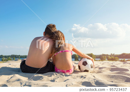 Children with a ball on the river bank on a sunny summer day. View from the back. The concept of sports and active games in the summer Children with a ball on the river bank on a sunny summer day. View from the back. The concept of sports and active games in the summer 95723437