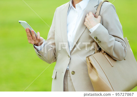 A middle-aged woman in a suit operating a smartphone in an outdoor park A middle-aged woman in a suit operating a smartphone in an outdoor park 95727867