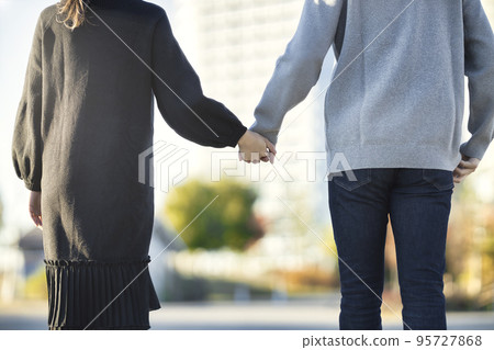 Back view of a couple wearing a coat and holding hands for a walk 95727868