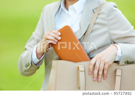 A middle-aged woman in a suit who takes out a wallet from her bag outdoors 95727892