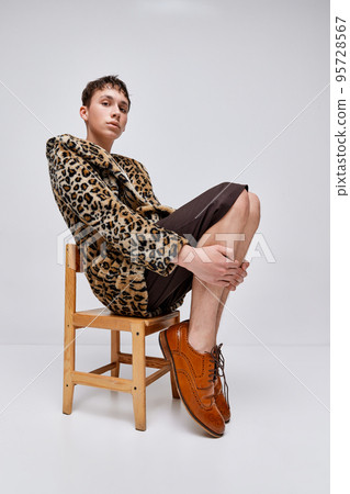 Portrait of stylish teen boy in animal print jacket and classic brogue shoes posing isolated on grey background. Tender look 95728567