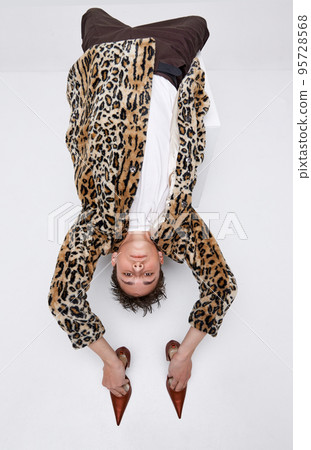 Portrait of stylish teen boy in animal print jacket and classic brogue shoes posing isolated on grey background. Weird pose 95728568