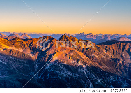 Alpine mountain peaks illuminated by rising sun Alpine mountain peaks illuminated by rising sun 95728781