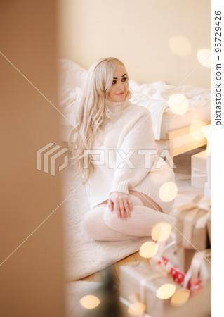 Portrait of Beautiful blond hair woman in pullover open present on Chrisrmas time. Elegant woman by Christmas tree. Attractive female hold present. Christmas mood. Winter holiday 95729426