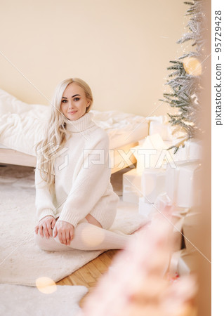 Portrait of Beautiful blond hair woman in pullover open present on Chrisrmas time. Elegant woman by Christmas tree. Attractive female hold present. Christmas mood. Winter holiday 95729428