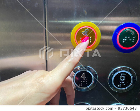 A woman's manicured finger on her hand presses a button in a modern beautiful elevator in a high-rise building 95730648